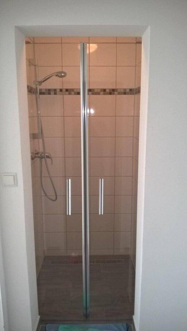 Duschbereich mit Glasabtrennung und hellen Fliesen, ausgestattet mit einer modernen Duschbrause.