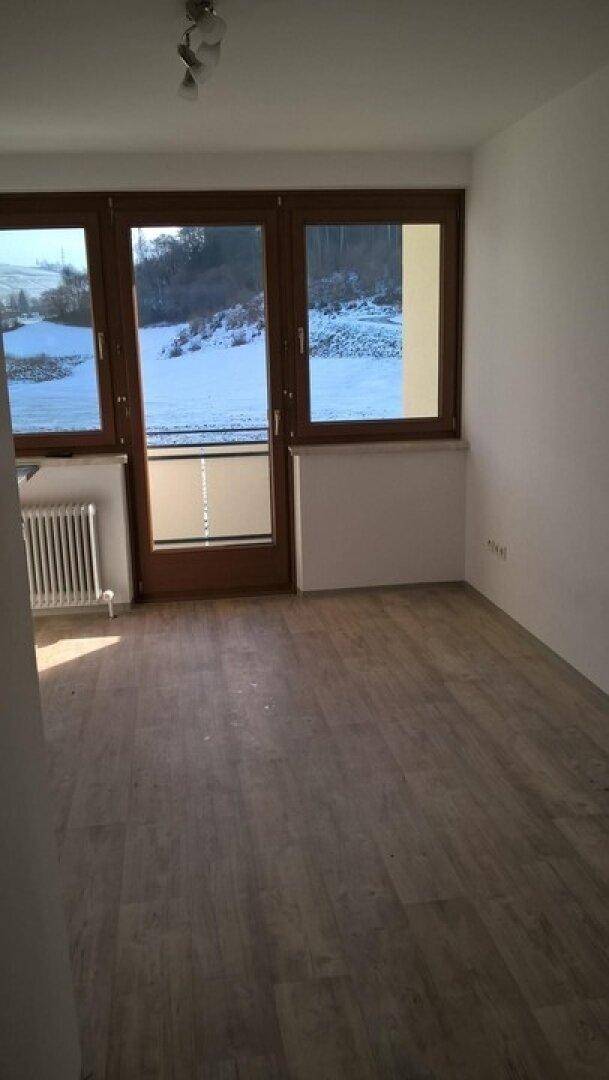 Heller Raum mit Holzboden und großen Fenstern, die einen weiten Blick auf eine verschneite Landschaft bieten.