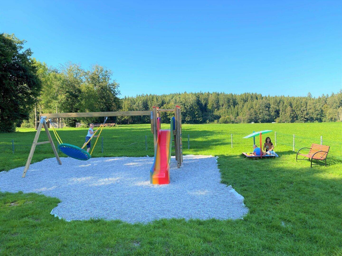 Großer Kinderspielplatz mit Schaukeln und Rutsche auf einer weitläufigen grünen Wiese.