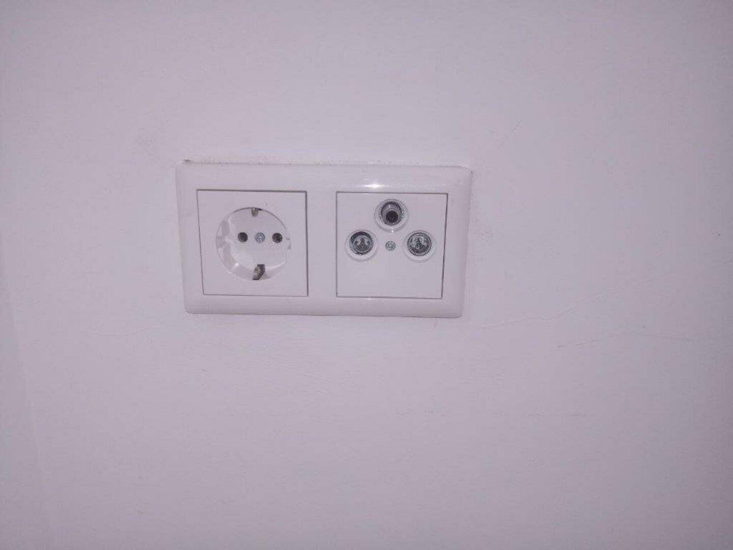 Weiße Steckdose und Antennenanschluss an einer hellen Wand.