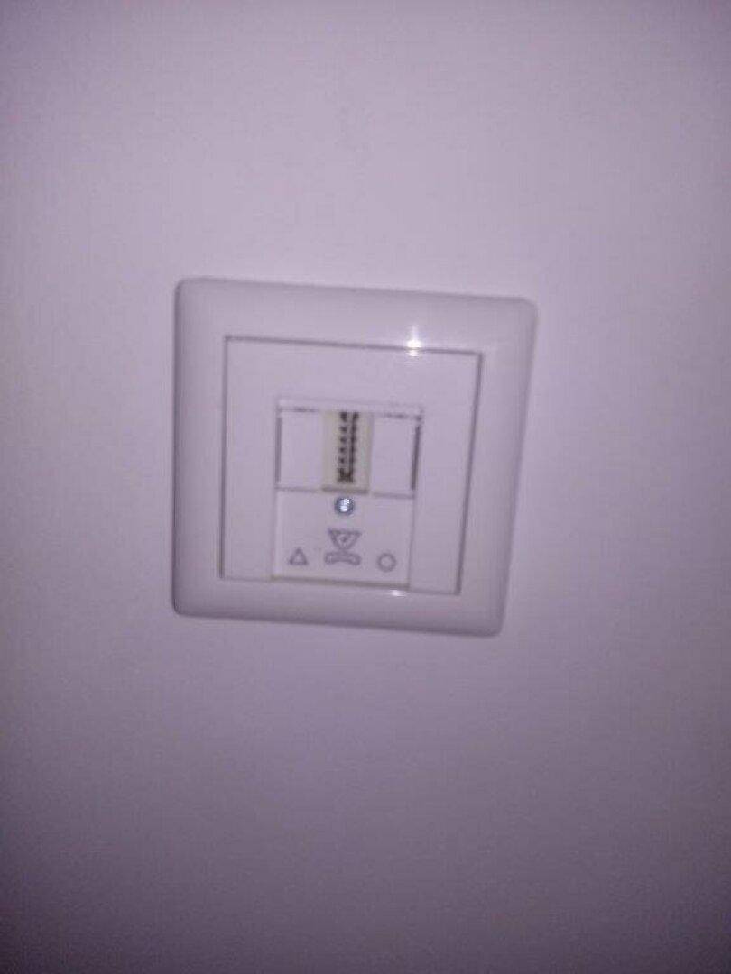 Nahaufnahme eines weißen Thermostats oder Lichtschalters an einer Wand.