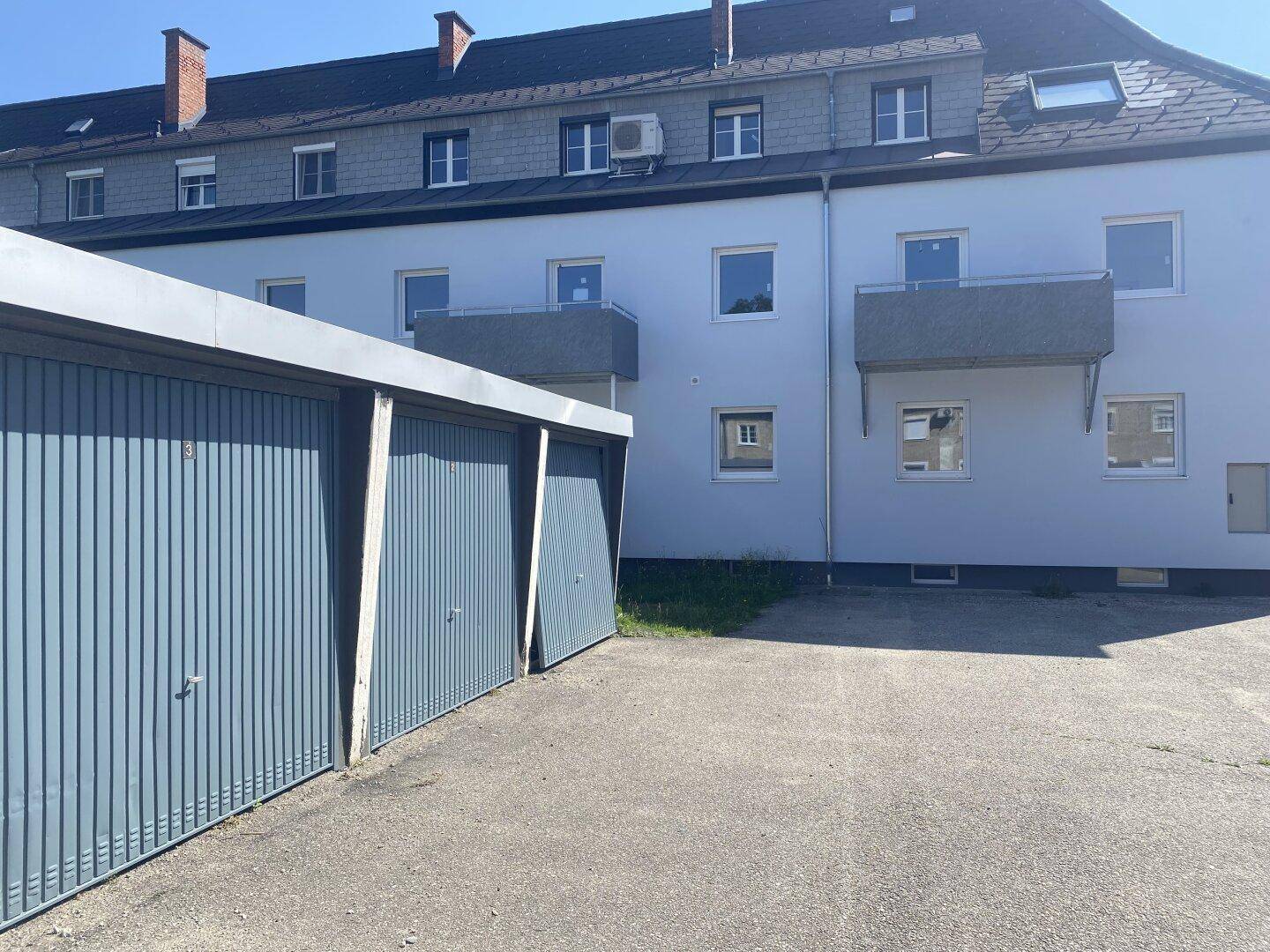 Außenansicht eines Mehrfamilienhauses mit Balkonen und davor liegenden Garagen.