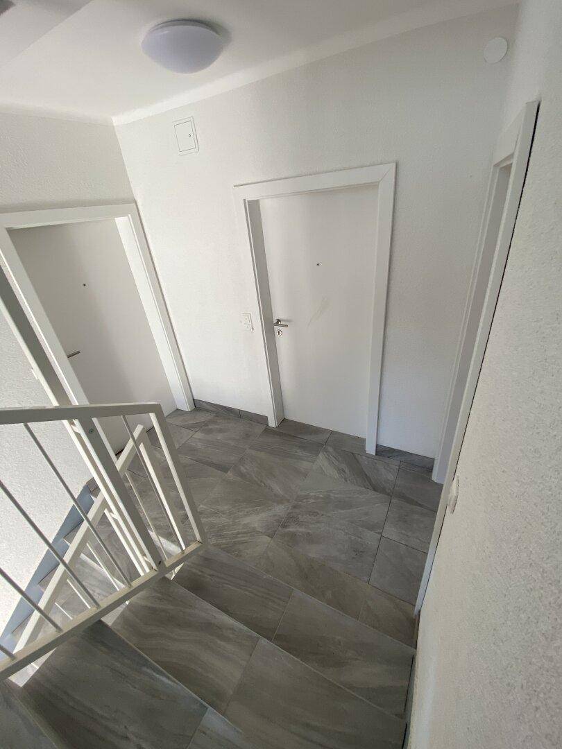 Heller Treppenaufgang mit modernen grauen Fliesen und weißem Geländer.