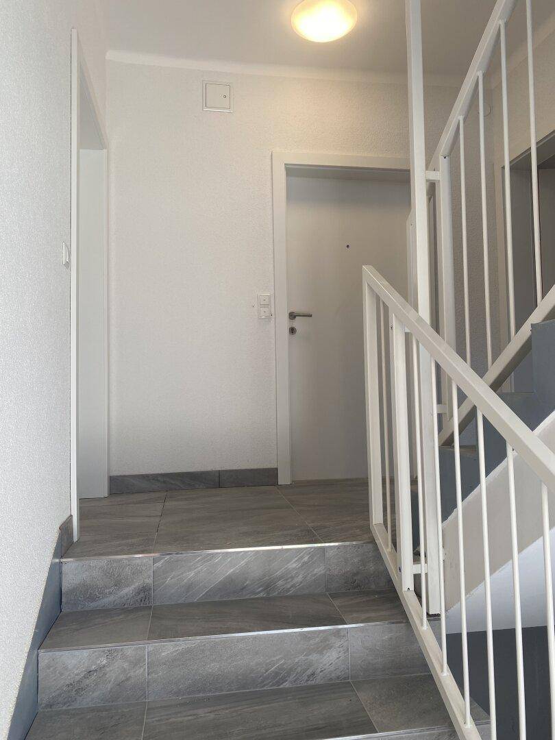 Treppenhaus mit grauen Fliesenstufen, weißem Geländer und einer Deckenleuchte.