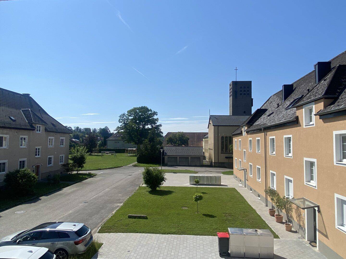 Außenansicht von Gebäuden mit traditionellen Dächern, einer Straße und einem Kirchturm im Hintergrund.