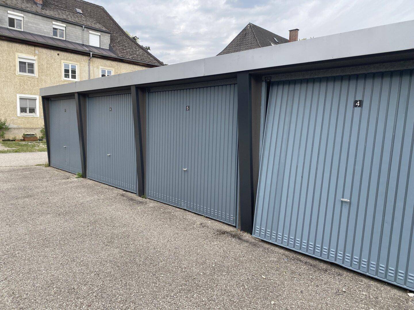 Reihe von Garagen mit blaugrauen Toren und einem asphaltierten Vorplatz.
