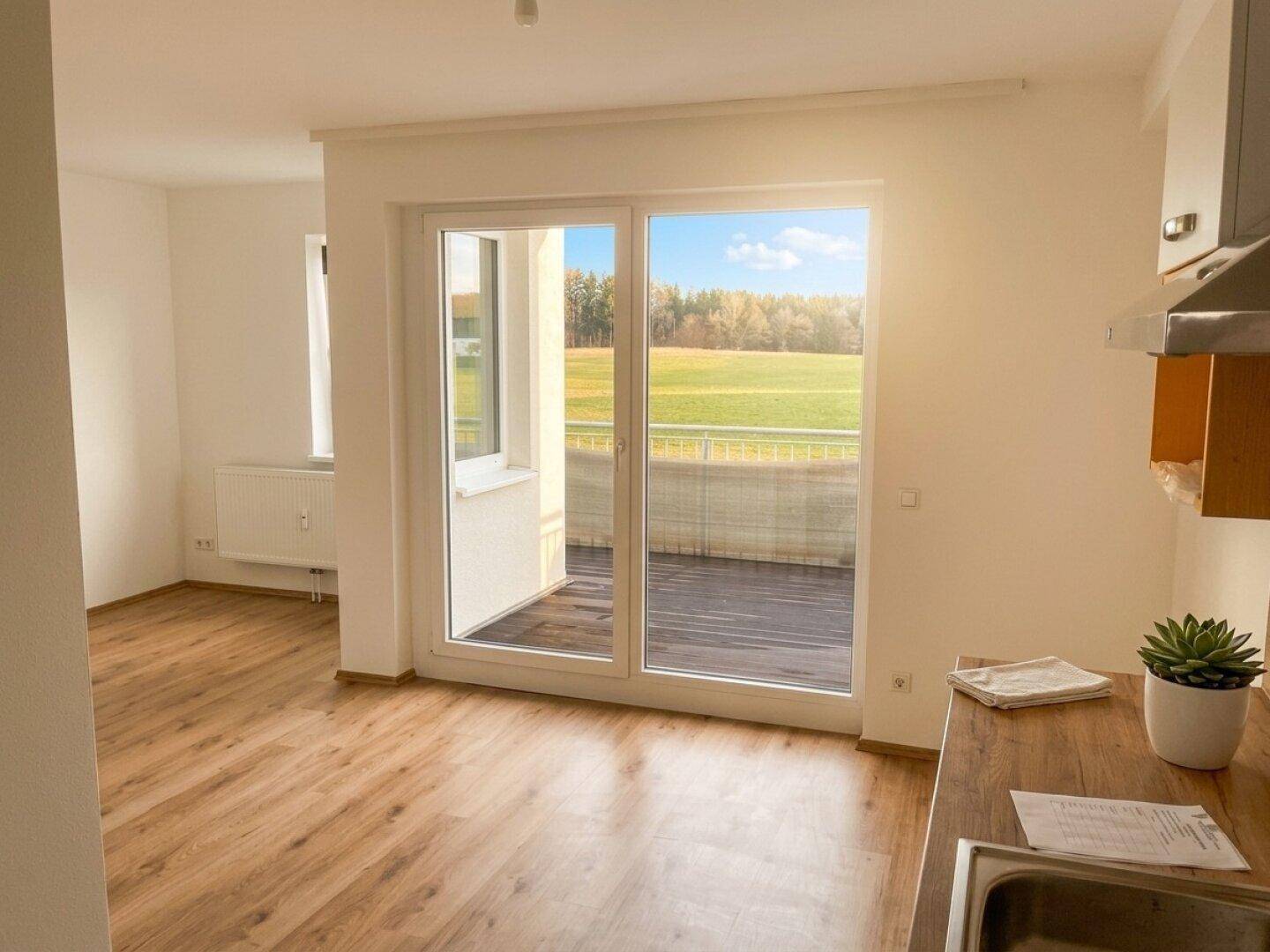 Helles Zimmer mit Holzboden, Zugang zum Balkon und weitem Blick ins Grüne.