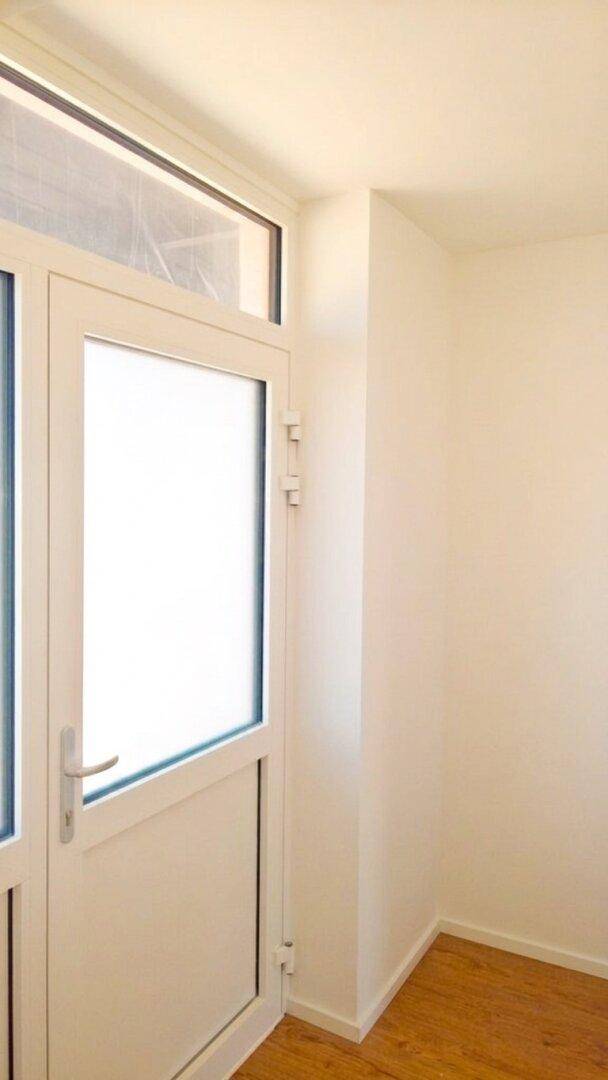 Weiße Tür mit Glaseinsatz und Holzboden in einem hellen Innenraum.