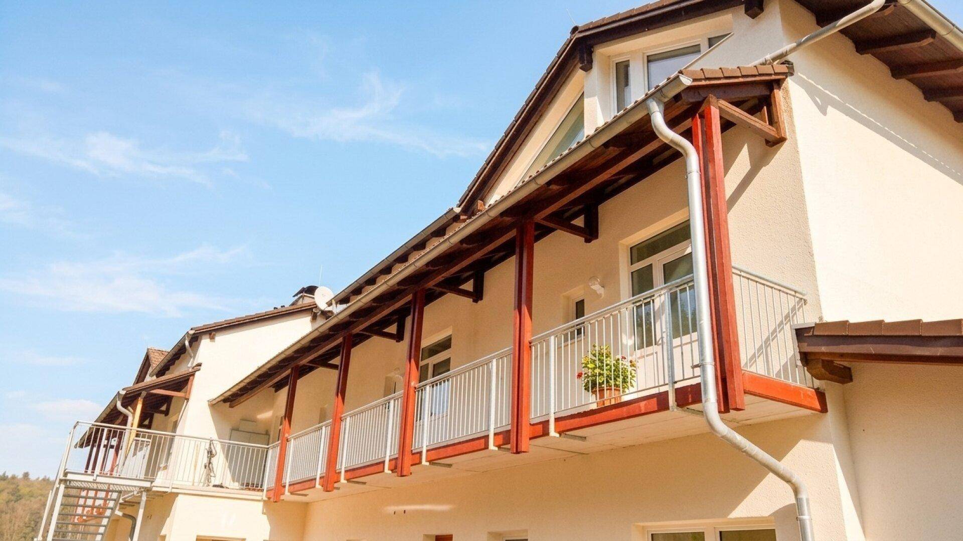 Fassade eines Gebäudes mit mehreren Balkonen, Holzkonstruktion und Metallgeländern unter blauem Himmel.