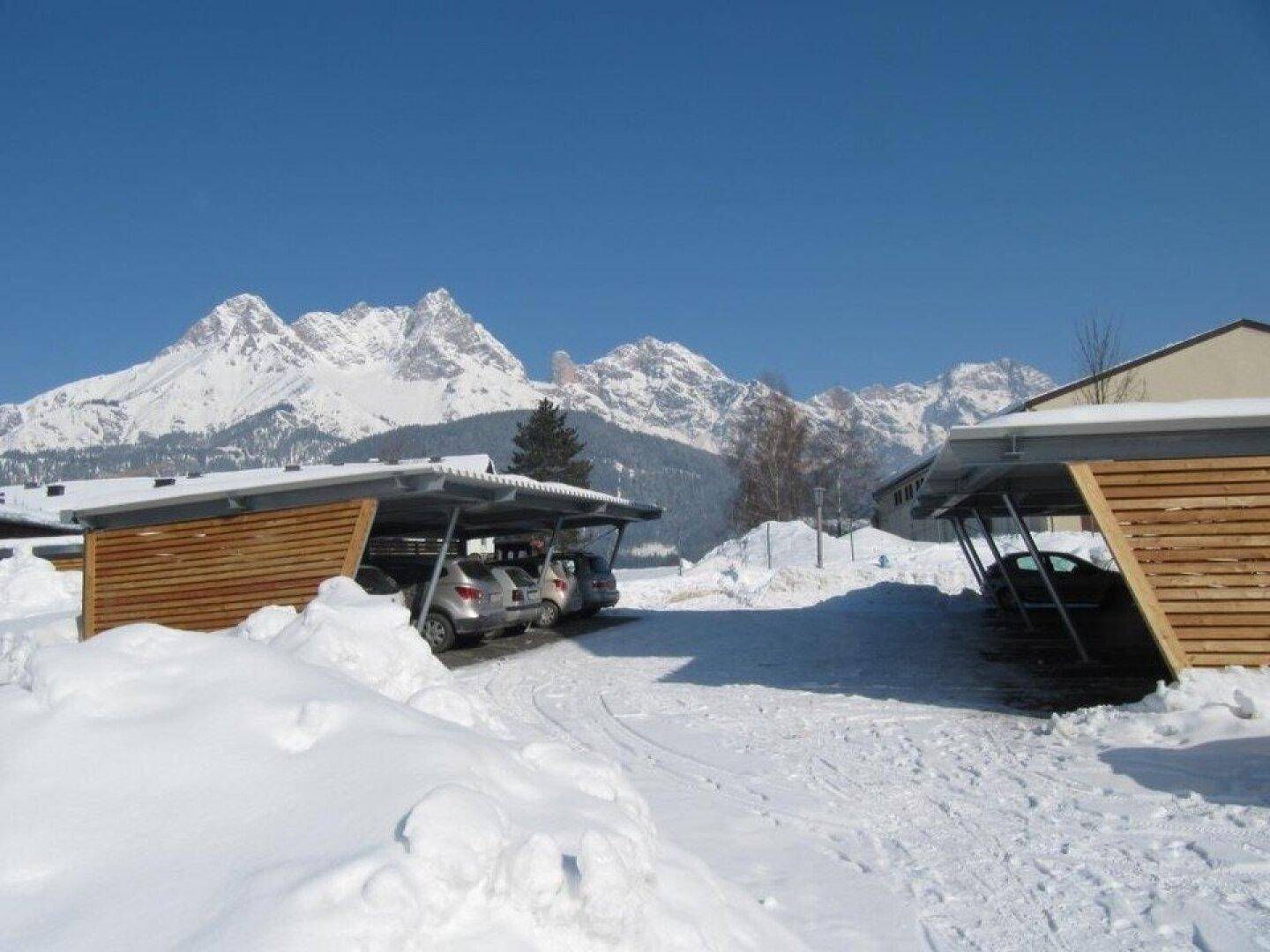 Carports im Schnee mit schneebedeckten Bergen im Hintergrund unter strahlend blauem Himmel.