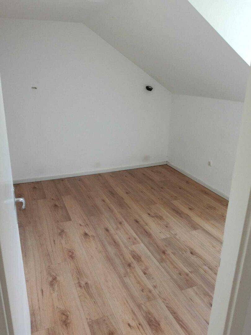 Leeres Zimmer mit Dachschräge und hellem Laminatboden, bereit zur individuellen Gestaltung.