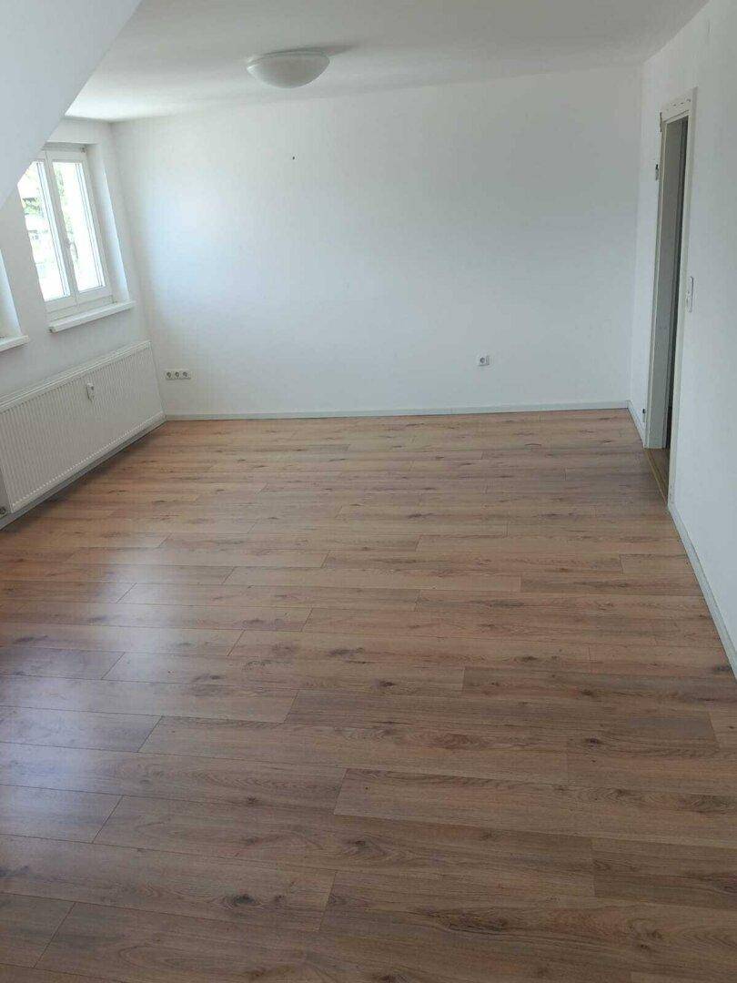 Helles, leeres Zimmer mit Laminatboden und Fenster, ideal für Wohn- oder Schlafbereich.