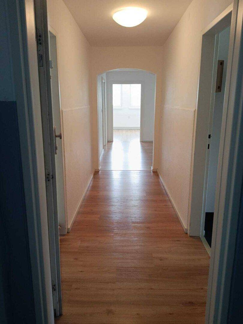 Langer Flur mit hellem Laminatboden und einem Bogen, der zu weiteren Räumen führt.