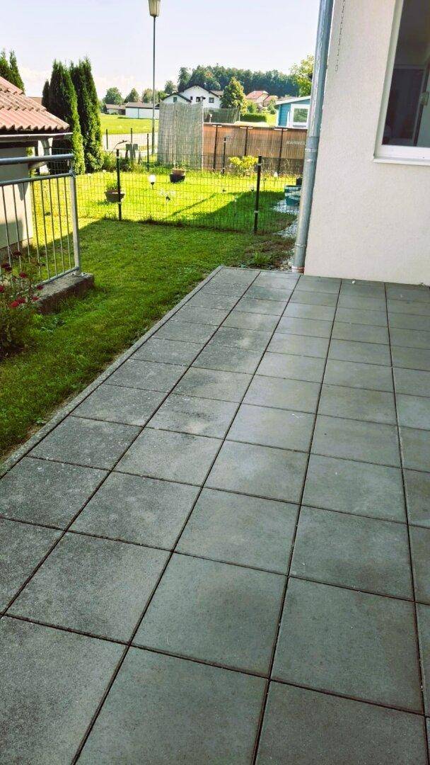 Helle gepflasterte Terrasse mit angrenzendem Rasen und Blick auf die Umgebung.