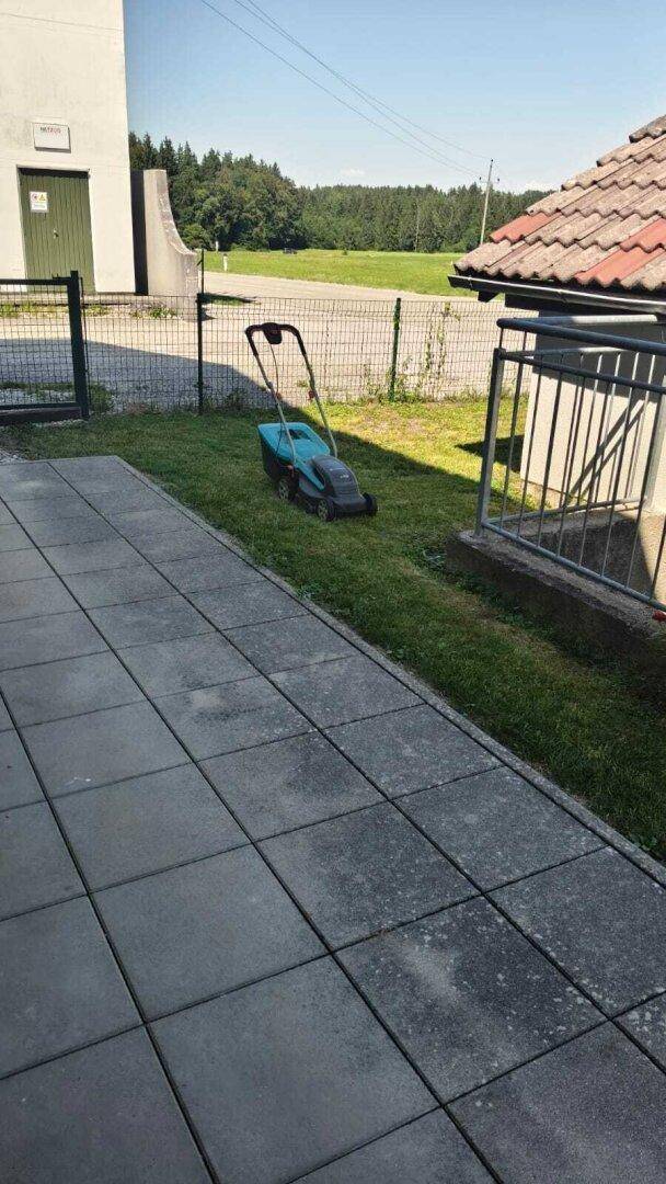 Gepflasterte Terrasse neben einem Rasen mit Rasenmäher und Blick ins Grüne.