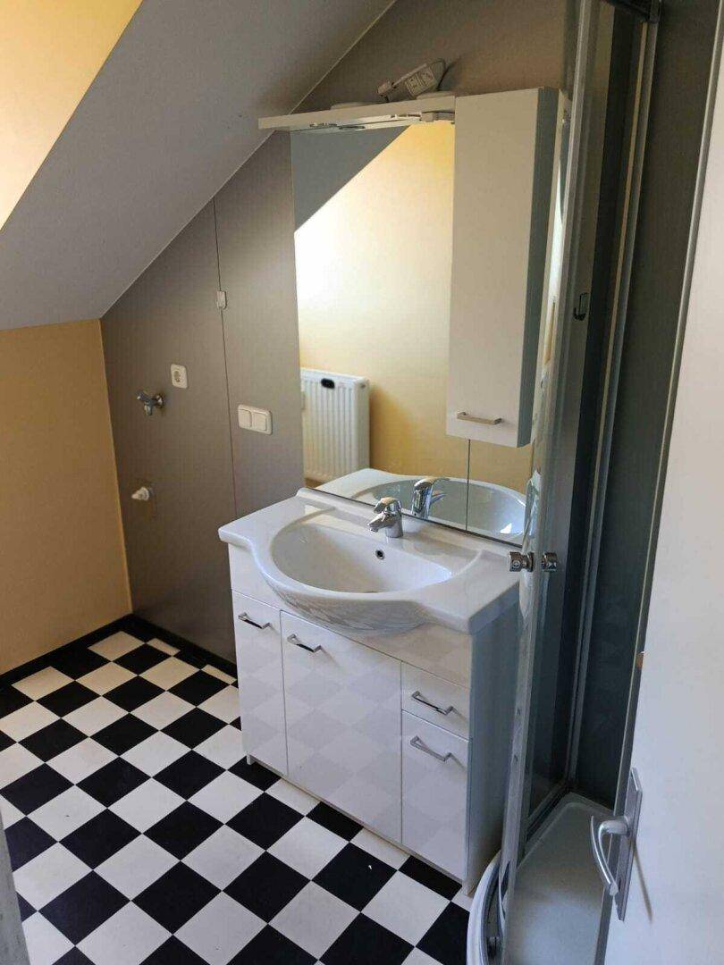 Badezimmer im Dachgeschoss mit Waschbecken, Spiegelschrank und schwarz-weiß kariertem Boden.