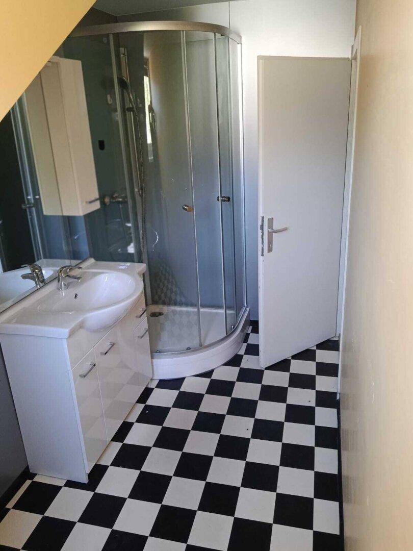 Badezimmer mit Eckdusche, Waschbecken und charakteristischem schwarz-weißem Fliesenboden im Dachgeschoss.