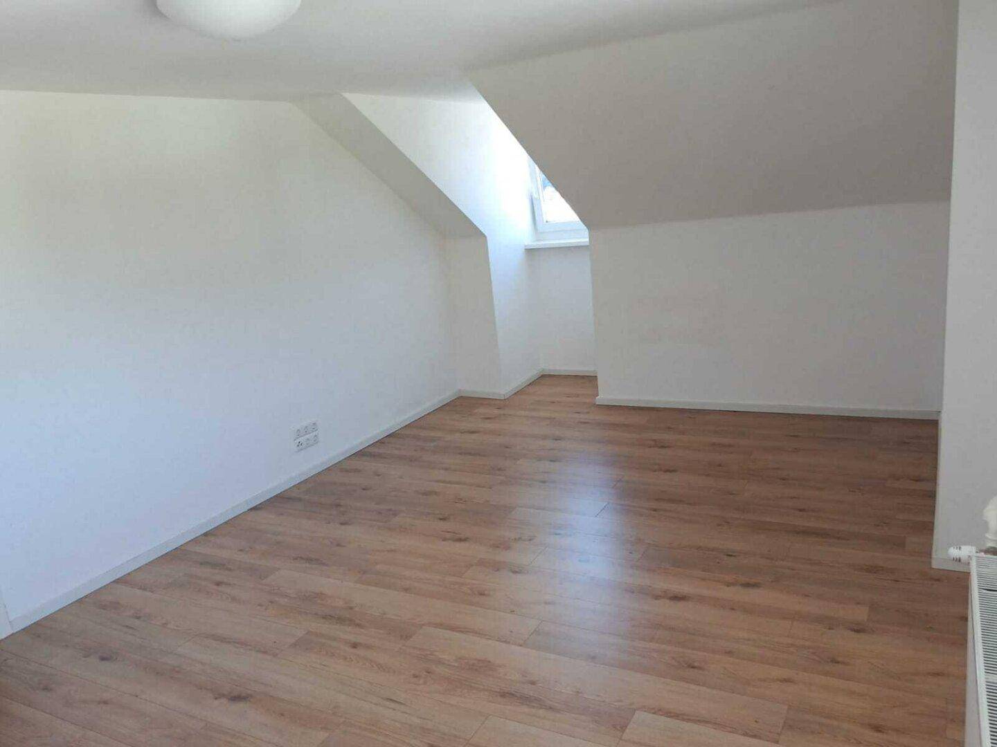 Heller Raum im Dachgeschoss mit Laminatboden, weißen Wänden und Dachfenster.