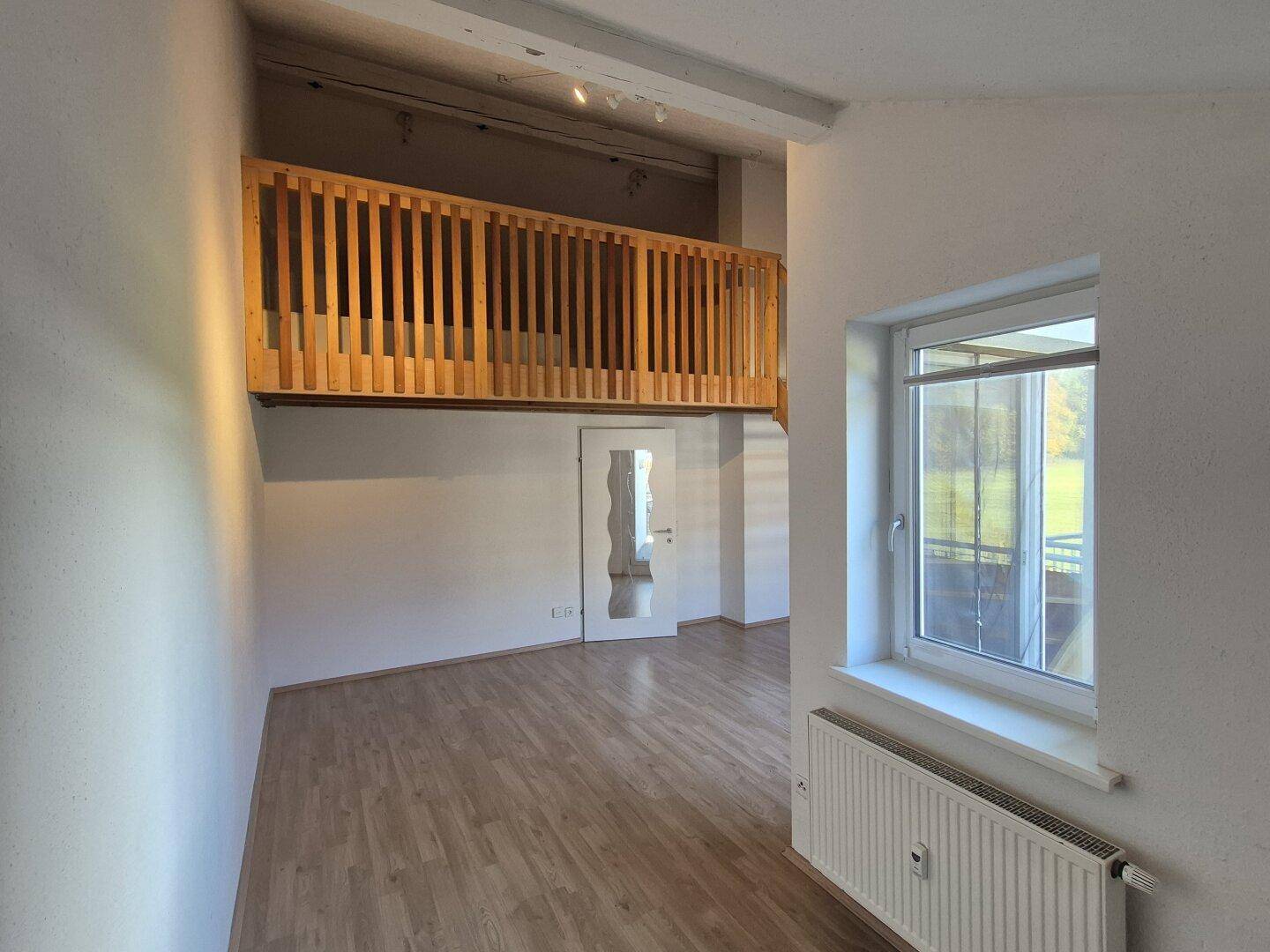 Geräumiger Wohnbereich mit Laminatboden, Fenster und Blick auf die Galerie.