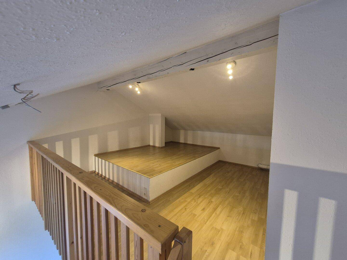 Dachgeschoss-Galerie mit Laminatboden, Holzgeländer und schrägen Wänden.