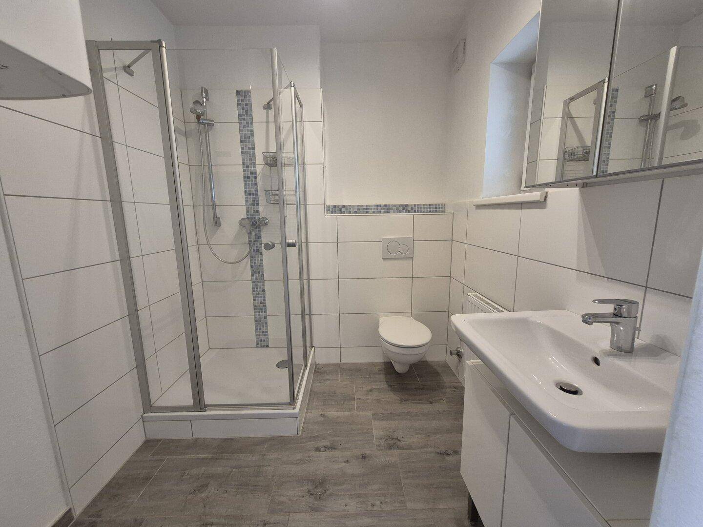 Helles Badezimmer mit Duschkabine, WC, Waschbecken und modernen Fliesen.