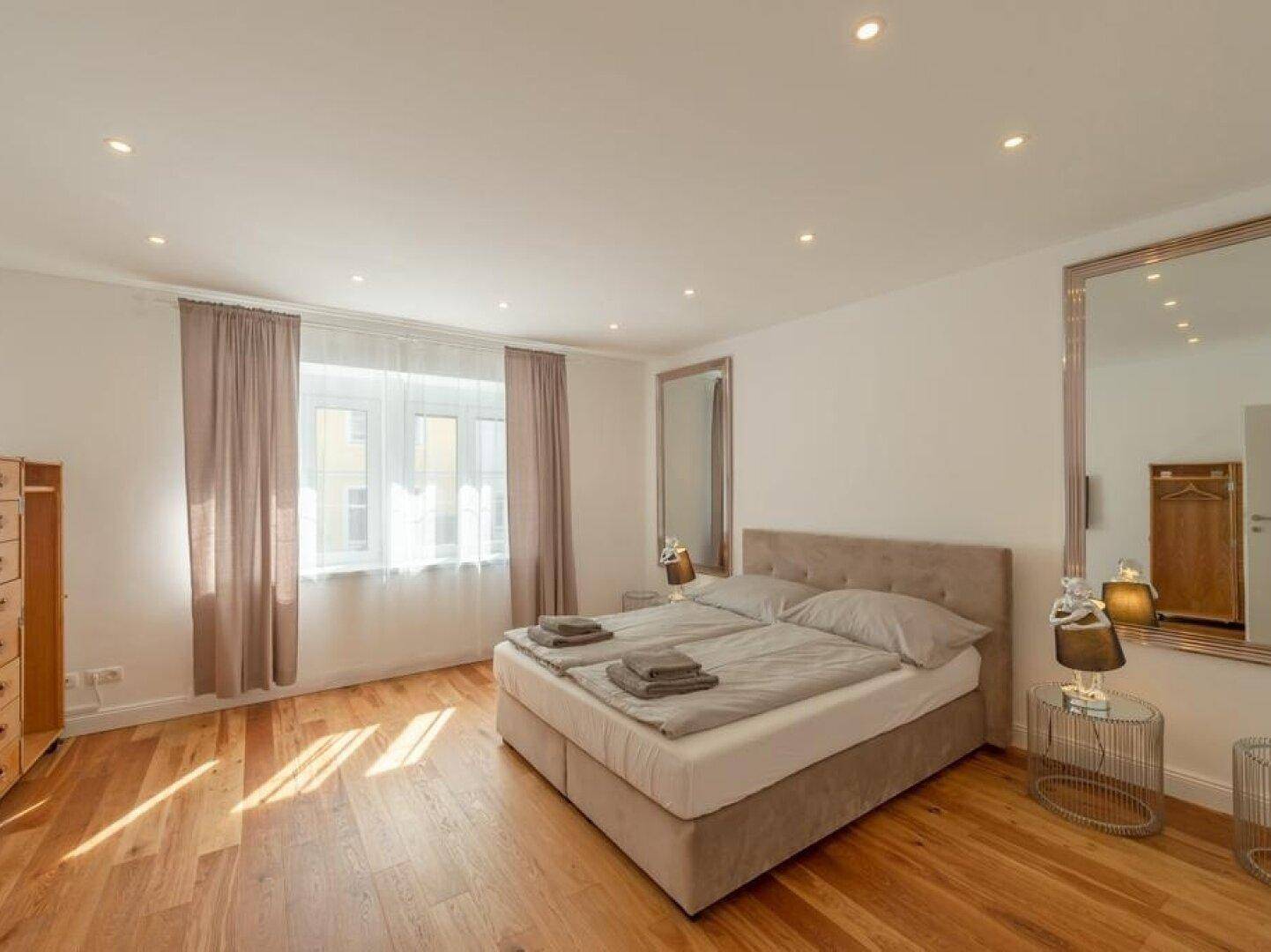 Helles Schlafzimmer mit Holzboden, Doppelbett und großem Spiegel.