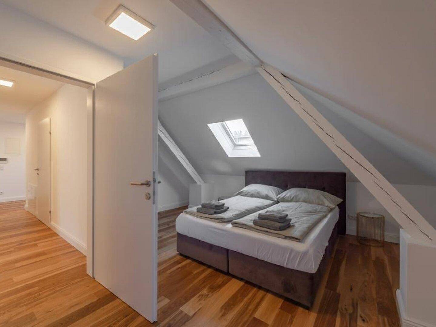 Schlafzimmer im Dachgeschoss mit Holzboden, Doppelbett und Dachfenster.