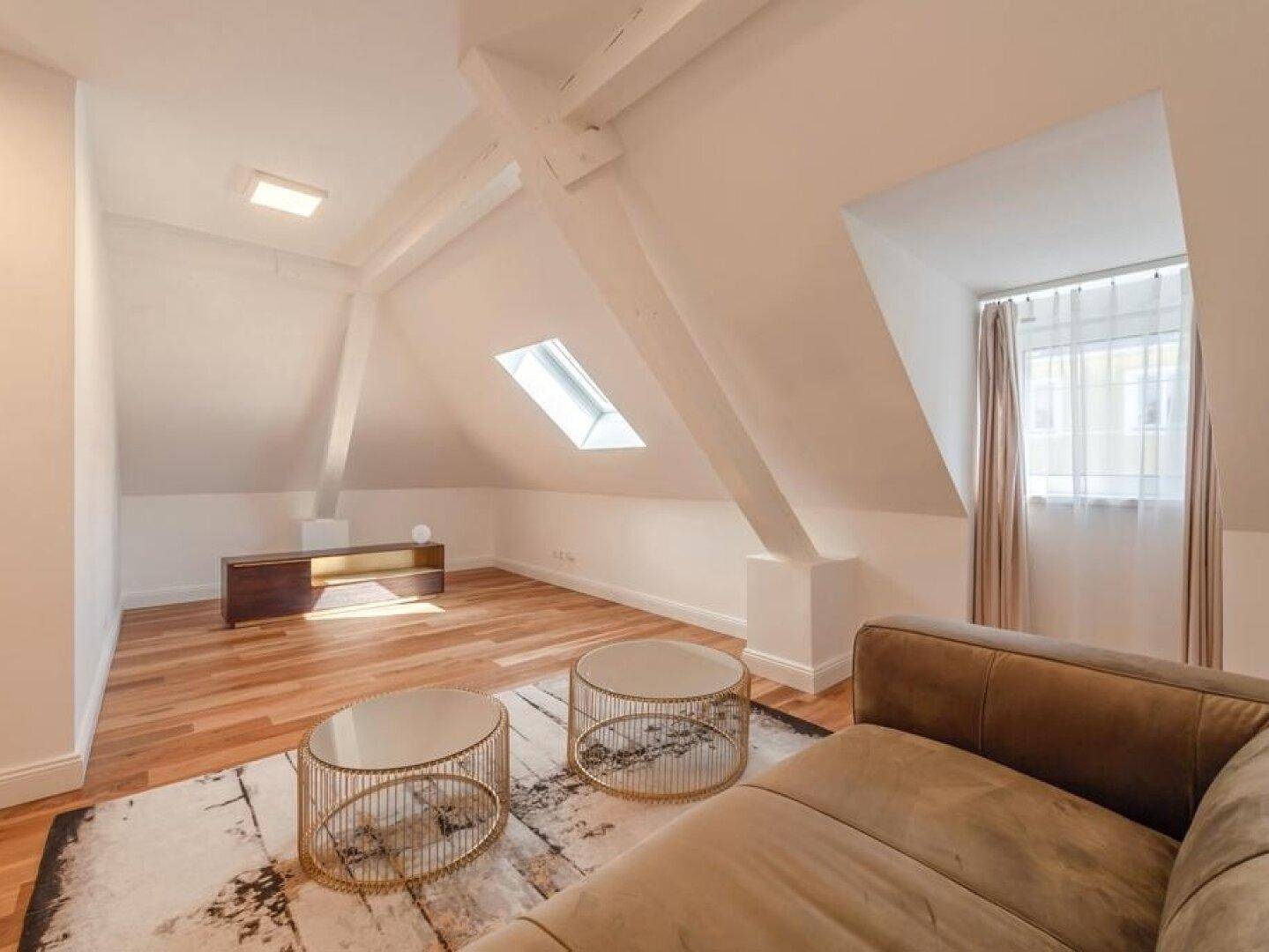 Geräumiger Wohnbereich im Dachgeschoss mit Holzboden, Dachfenster und sichtbaren Balken.