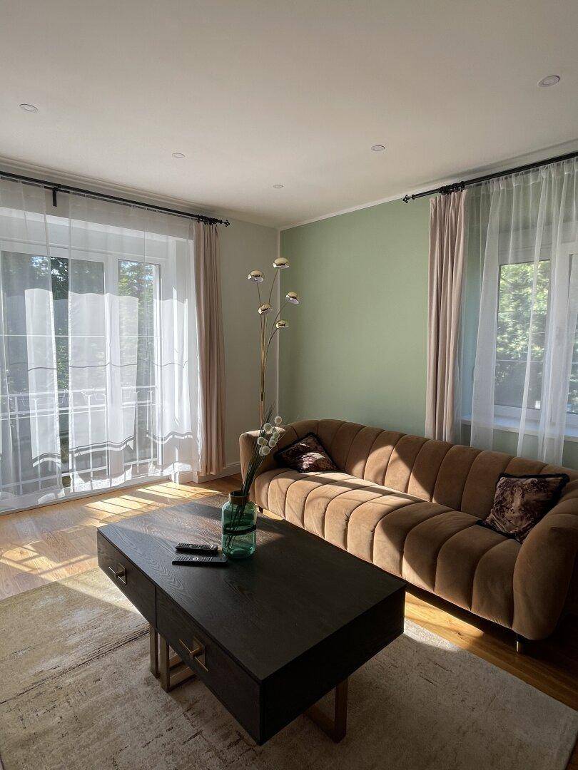 Gemütliches Wohnzimmer mit Balkonzugang, Holzboden und sanfter Wandfarbe.