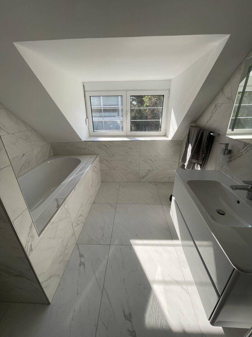 Modernes Badezimmer im Dachgeschoss mit Badewanne, Waschtisch und Fenster.