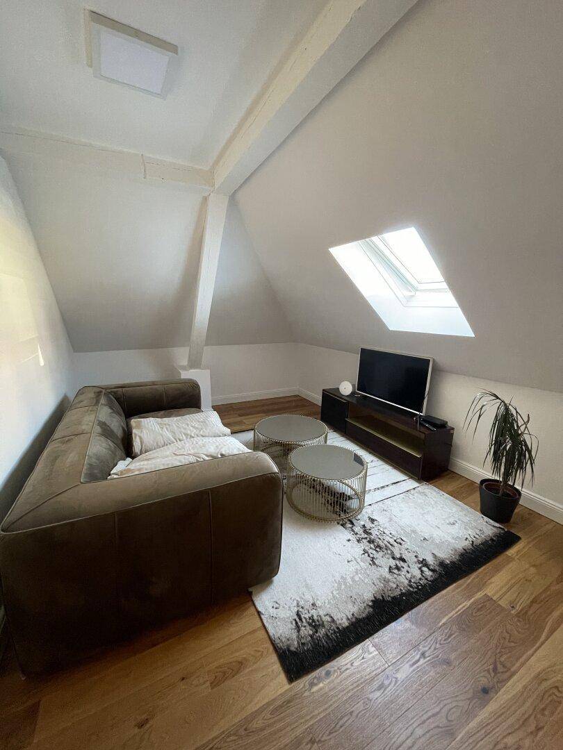 Dachgeschoss-Wohnzimmer mit gemütlichem Sofa, Fernseher und Holzboden.
