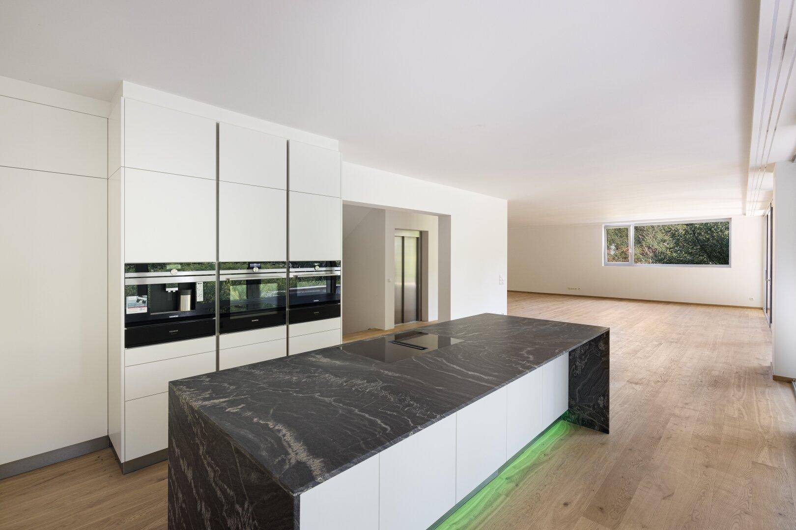 Moderne Küche mit weißer Einbauküche, dunkler Arbeitsplatte und integrierten Geräten.