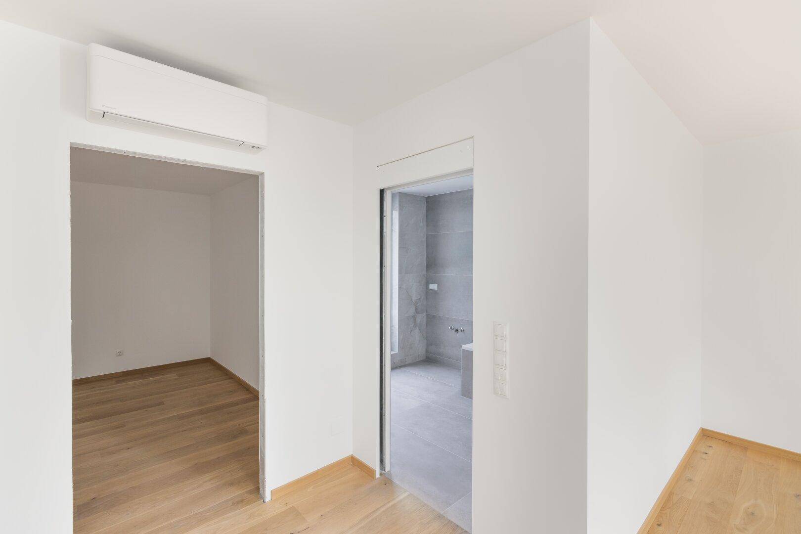 Heller Flur mit Zugang zu einem Zimmer und einem modernen Badezimmer mit Klimaanlage.