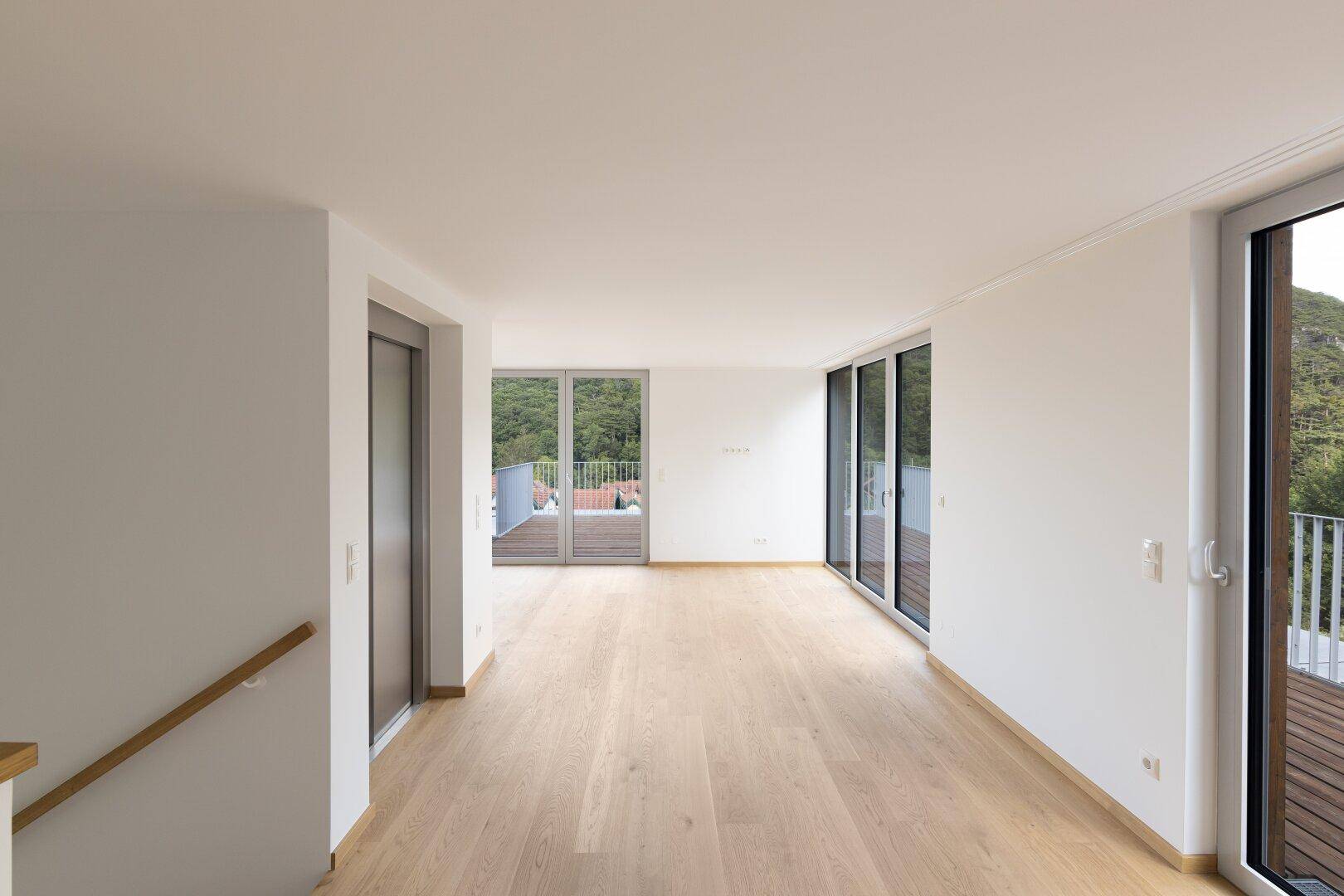 Geräumiger Wohnbereich mit Holzboden, großen Fenstern und Zugang zu mehreren Terrassen.