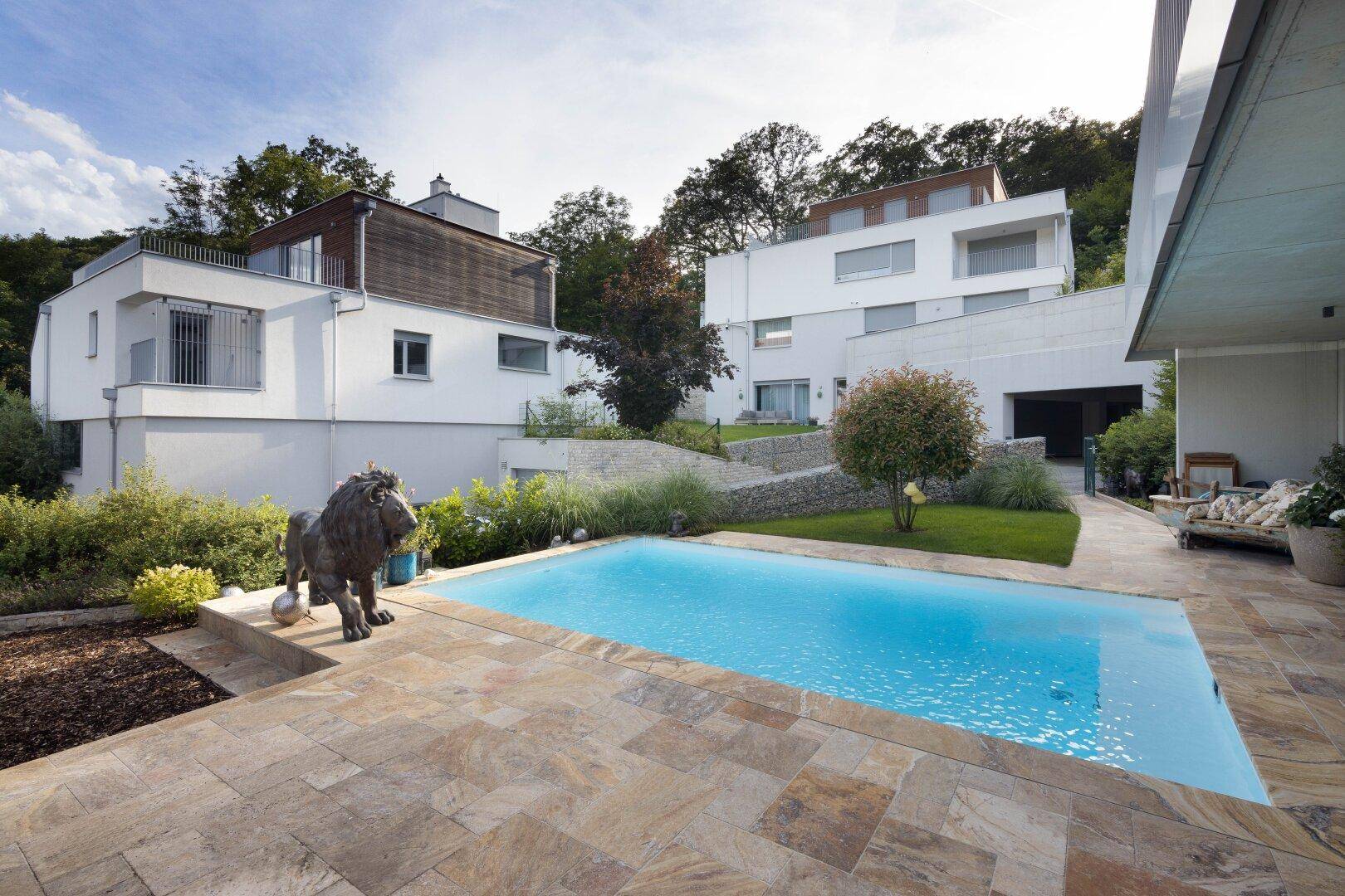 Außenbereich mit Swimmingpool, gepflasterter Terrasse und modernen Wohnhäusern im Hintergrund.