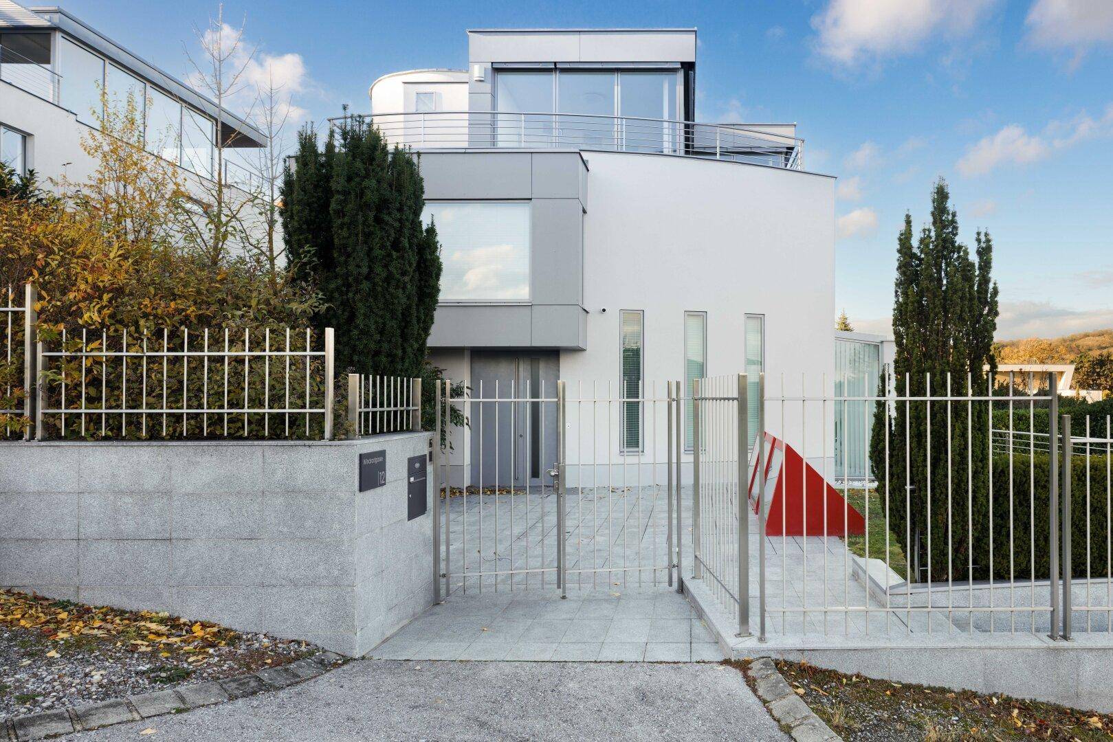 Moderne Villa mit eleganter Fassade, großem Eingangstor und gepflegter Zufahrt.