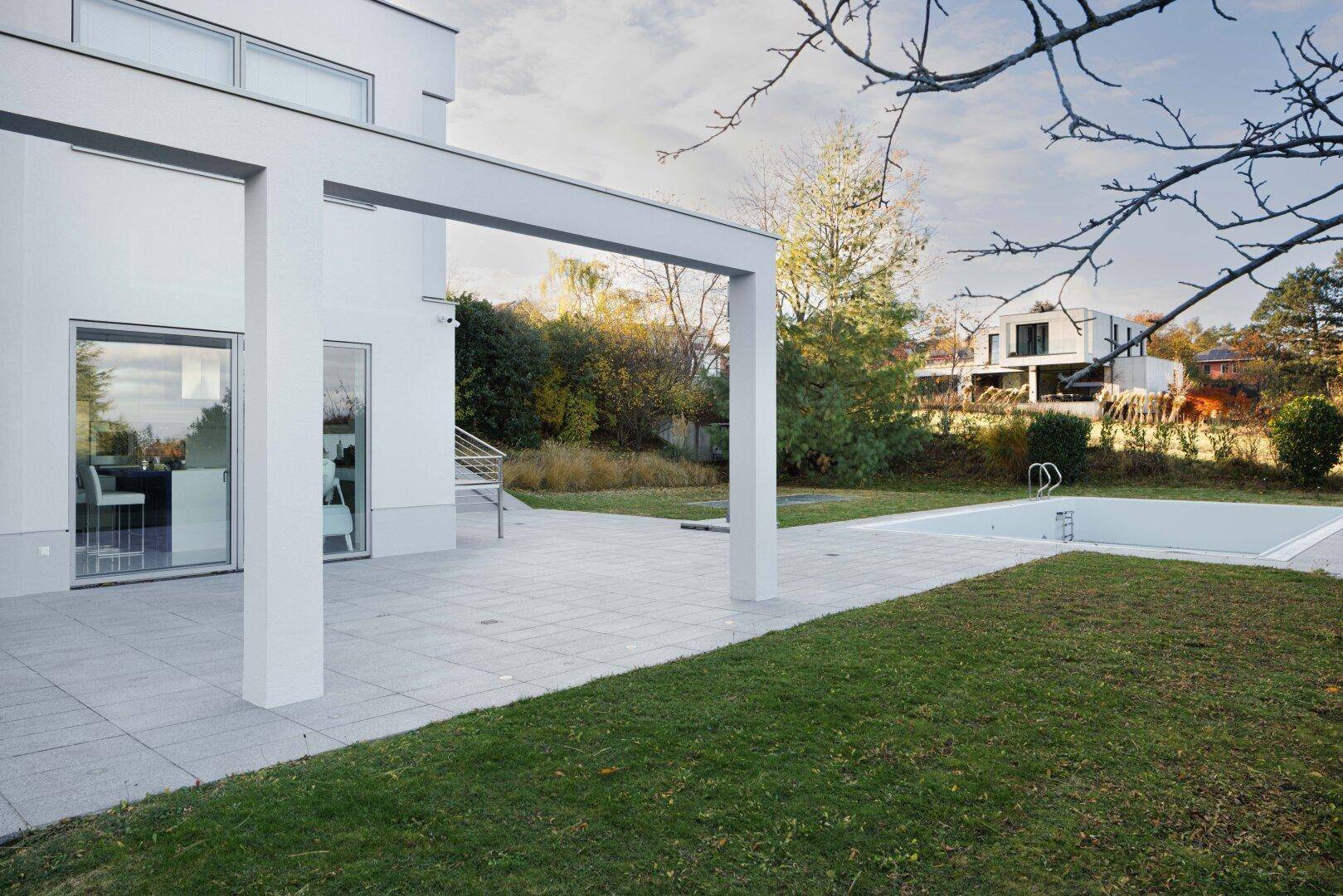 Gepflegter Gartenbereich mit Rasenfläche, Terrasse und einem leeren Außenpool.
