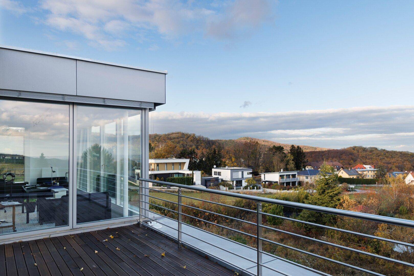 Großer Balkon mit Holzboden und weitem Blick über die umliegende Landschaft und Häuser.