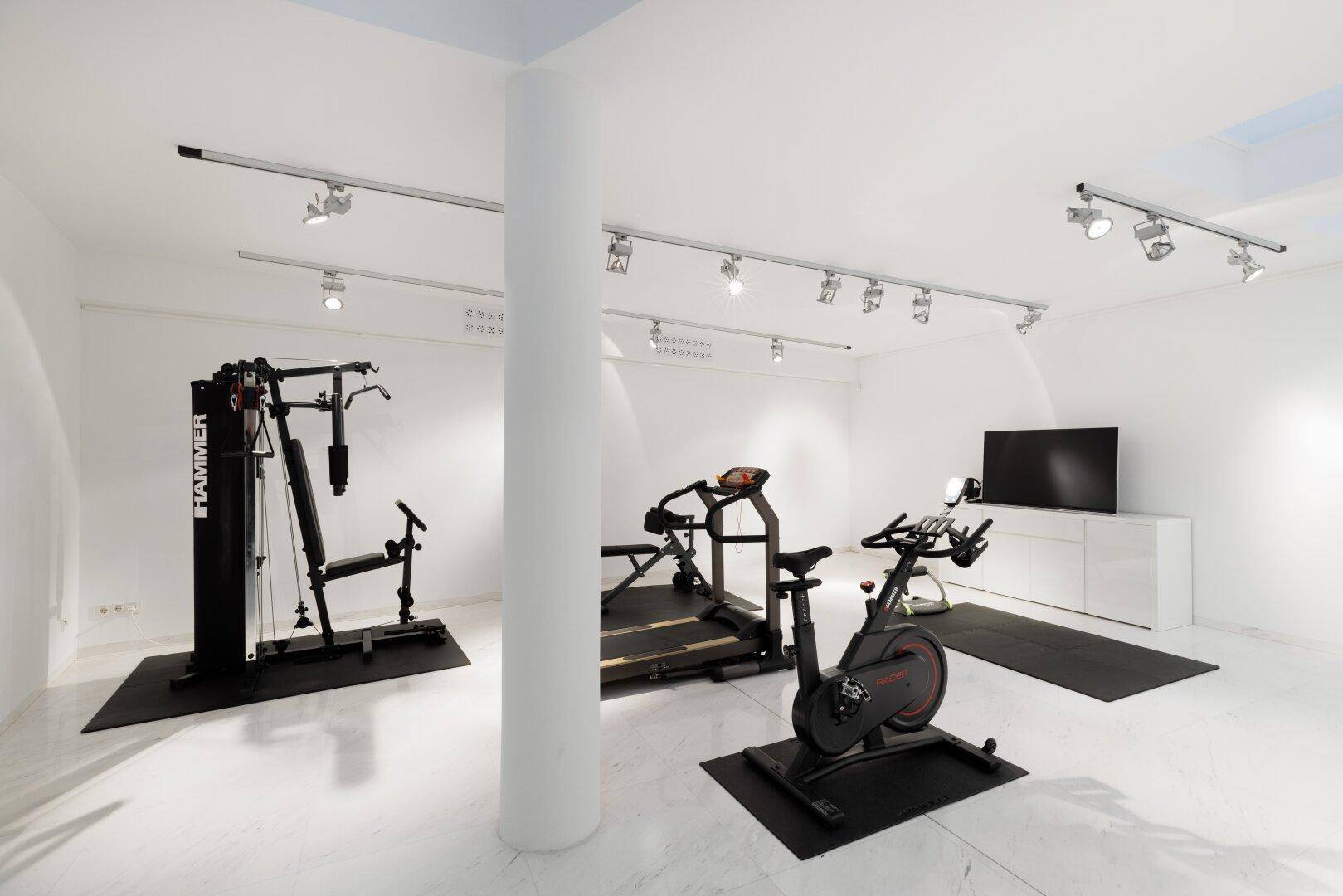 Gut ausgestatteter Fitnessraum mit verschiedenen Trainingsgeräten und hellem Ambiente.