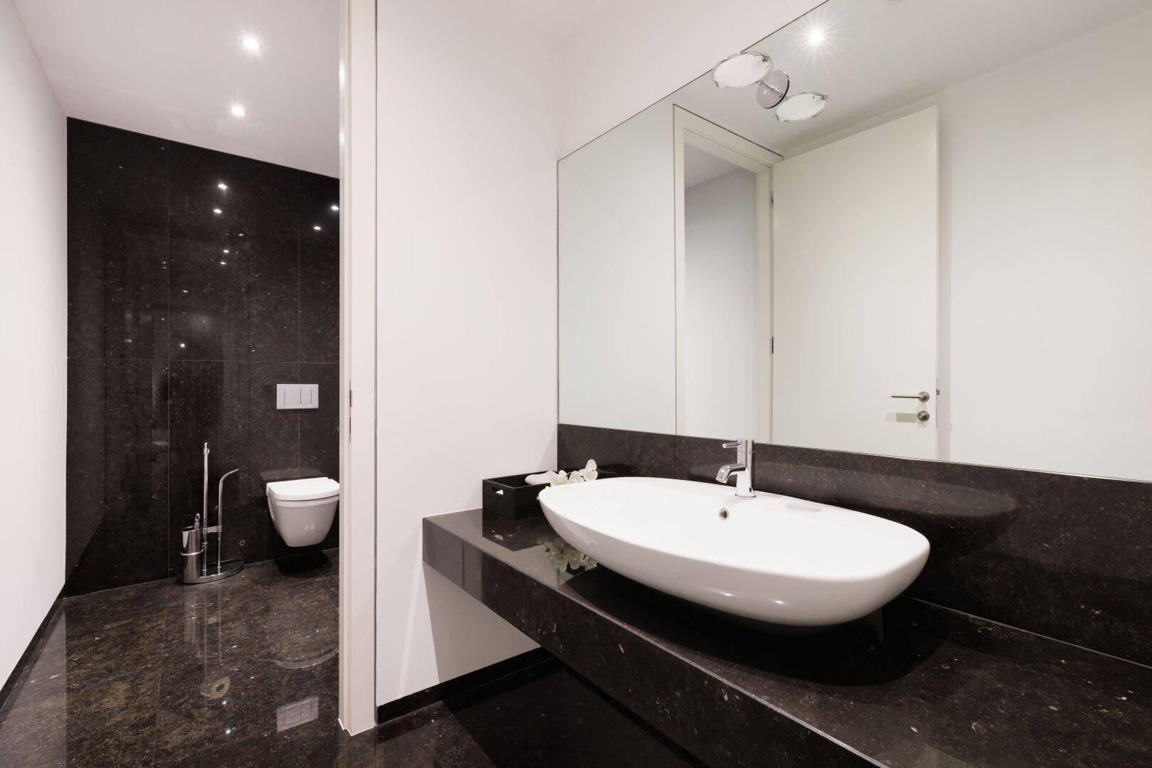 Modernes Badezimmer mit dunklen Granitfliesen, wandmontierter Toilette und Einzelwaschbecken.