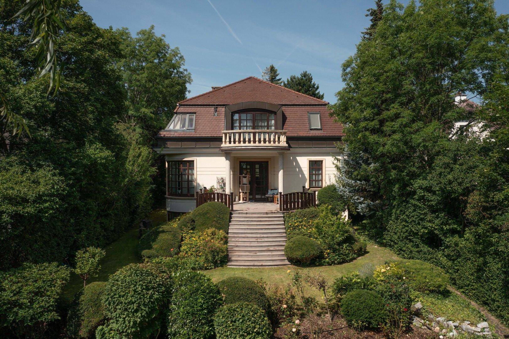 Beeindruckende Villa mit weitläufigem, terrassiertem Garten und üppiger Bepflanzung unter blauem Himmel.