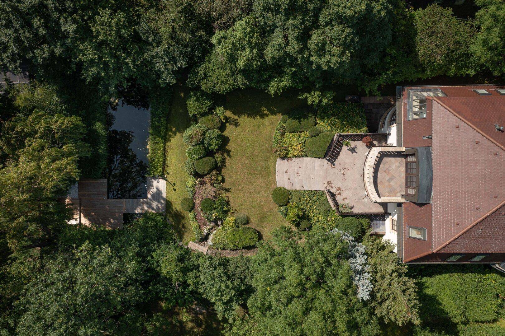 Luftaufnahme der Villa mit weitläufigem Garten, Teich und Terrasse, umgeben von dichtem Grün.