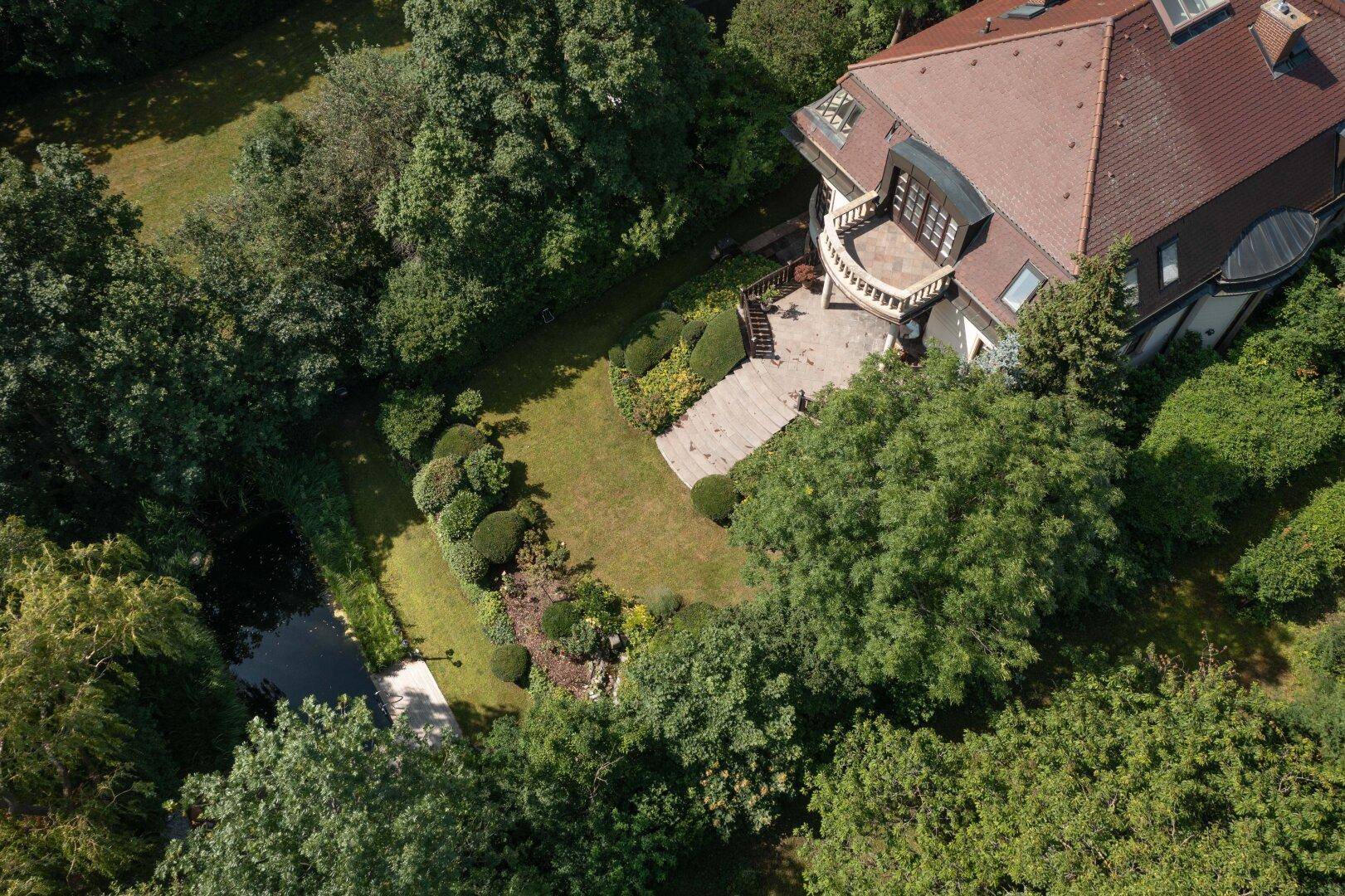 Vogelperspektive der Villa mit großem Garten, Teich und Terrasse, eingebettet in grüne Natur.