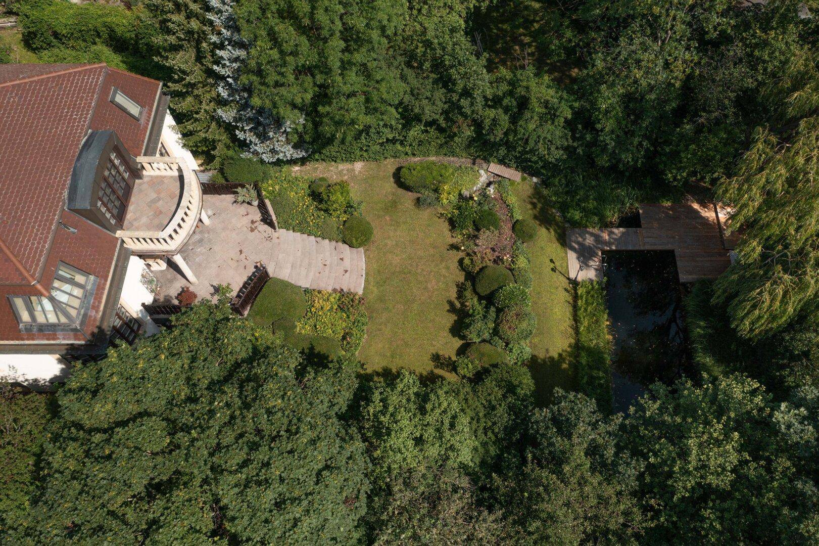 Übersicht der Villa von oben mit gepflegtem Garten, Teich und großzügiger Terrasse.