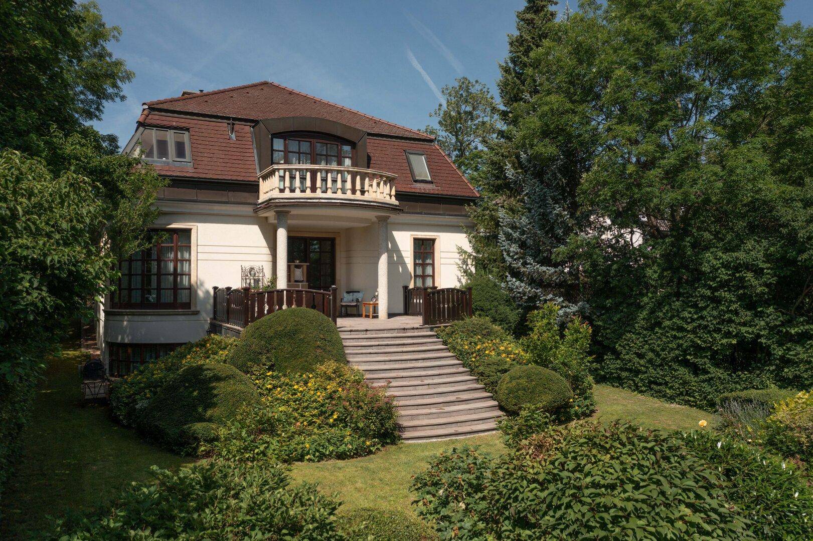 Klassische Villa mit großzügiger Steintreppe und gepflegtem Garten unter strahlend blauem Himmel.