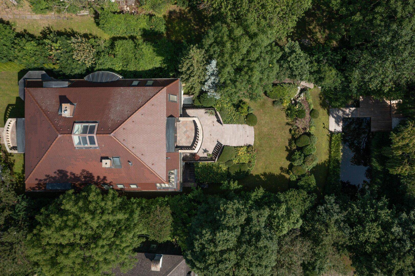 Dachansicht der Villa mit weitläufigem Garten, Teich und Terrasse, umgeben von Bäumen.