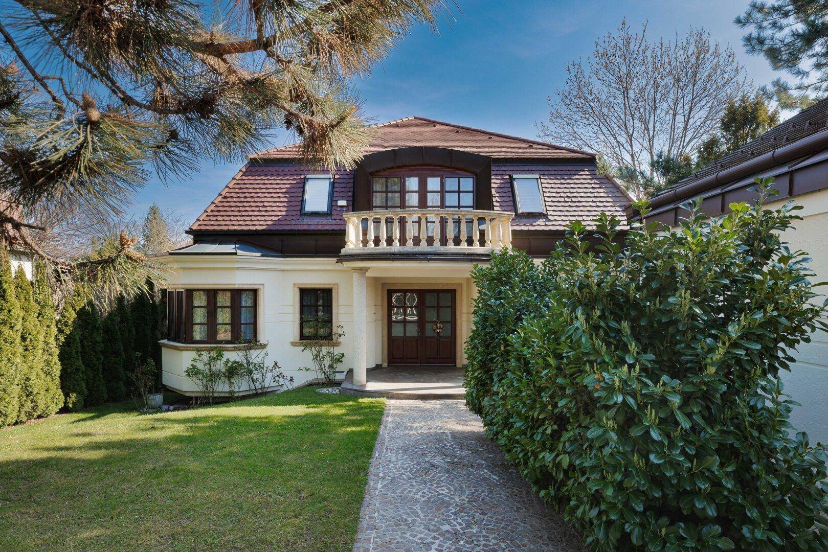 Charmante Villa mit gepflegtem Vorgarten und Steinweg, umgeben von grünen Hecken.