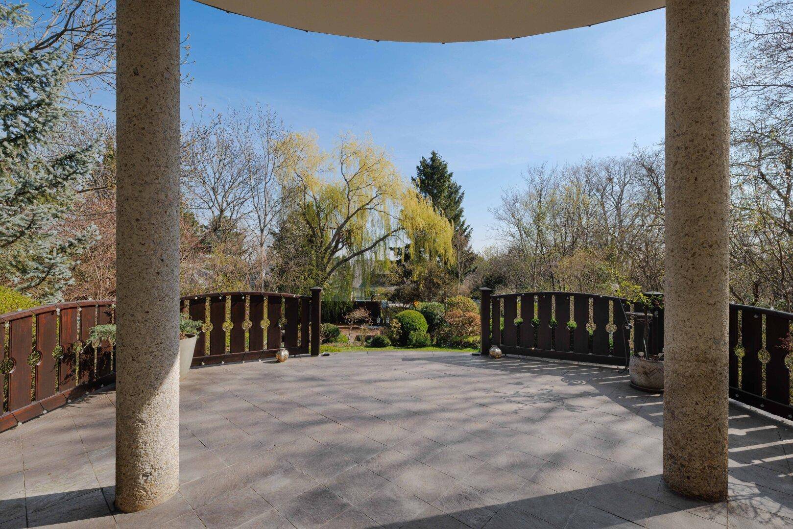 Große, überdachte Terrasse mit Steinsäulen und weitem Blick in den grünen Garten.