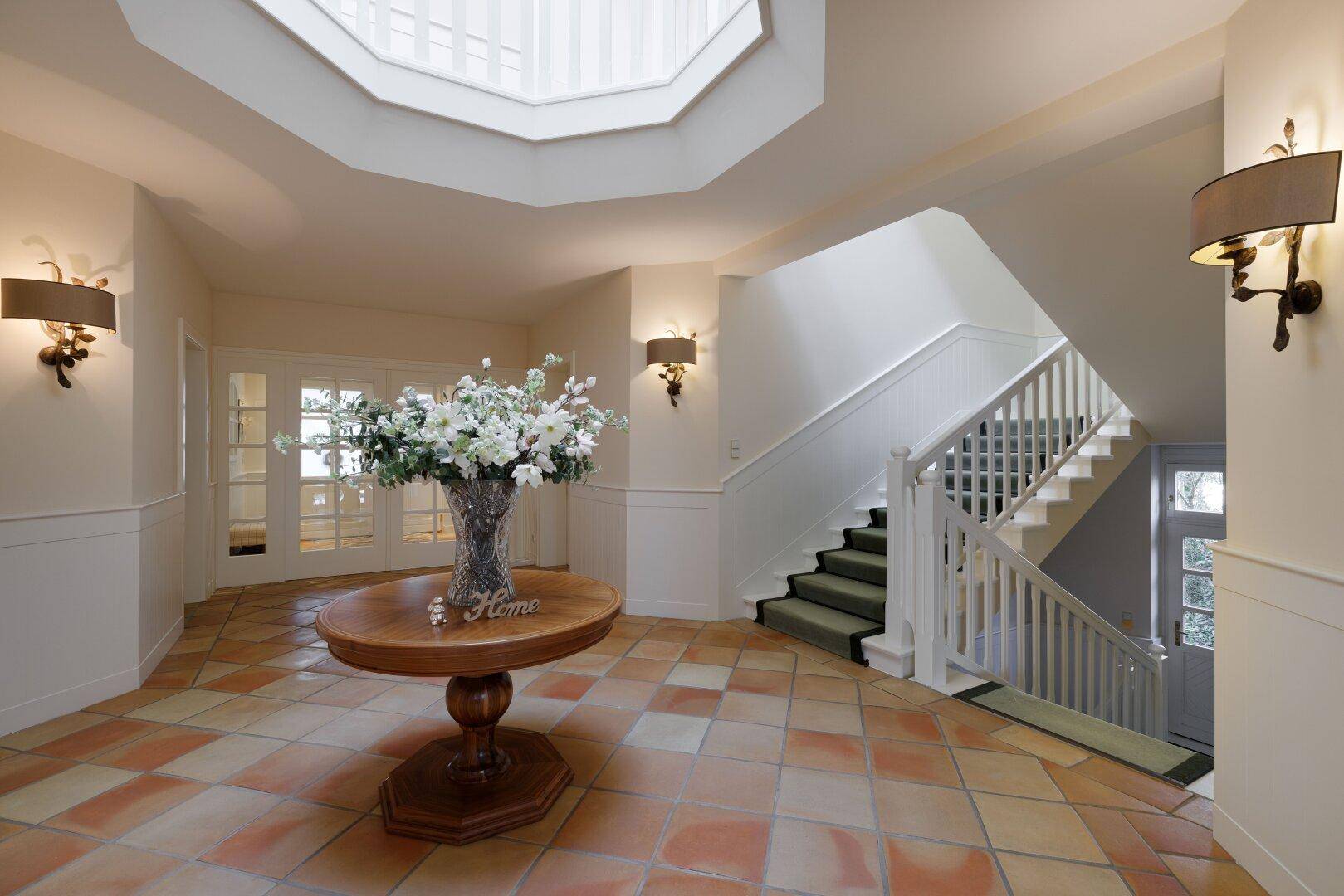 Heller Eingangsbereich mit Terrakottaboden, eleganter Treppe und Oberlicht.