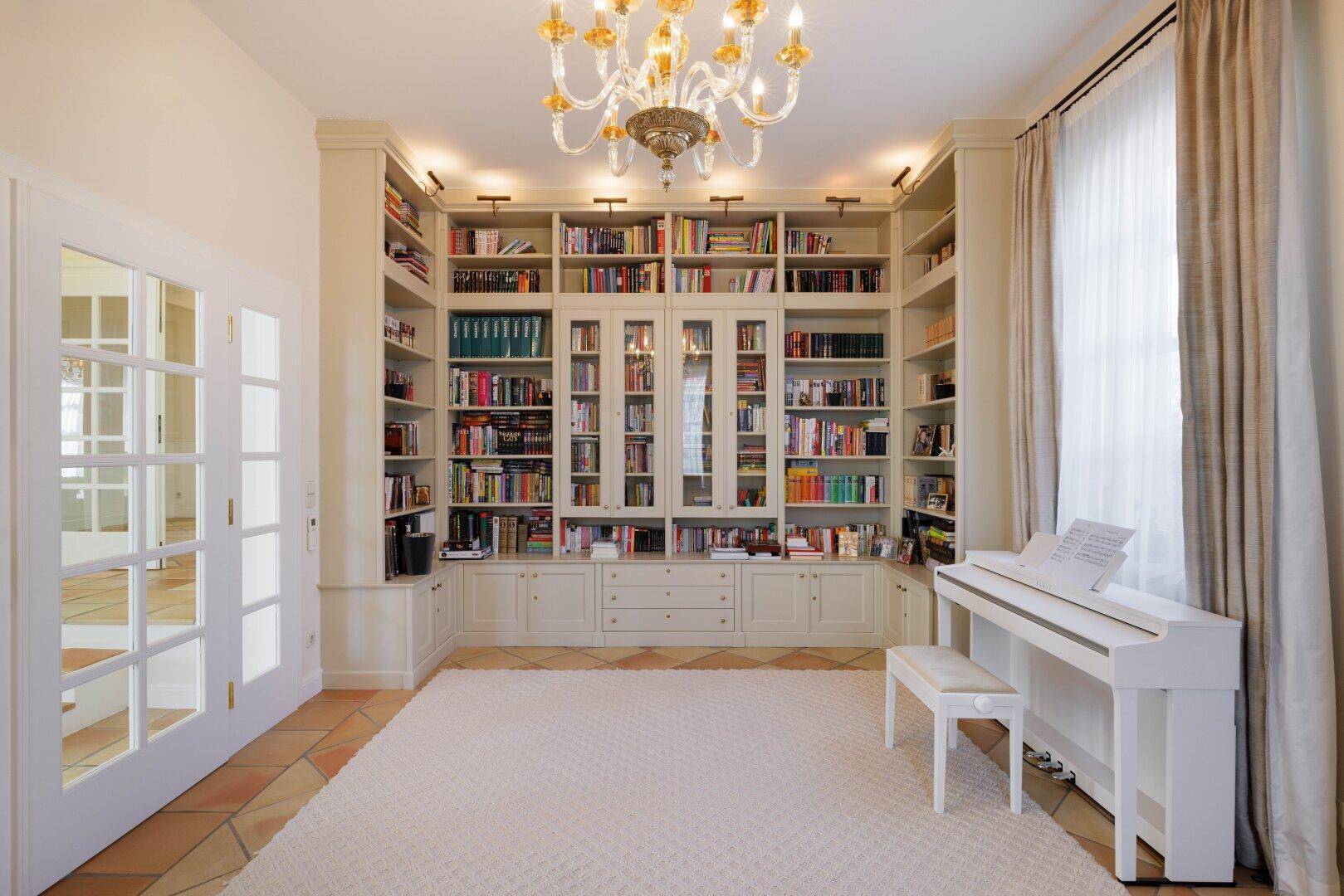 Stilvolle Bibliothek mit raumhohen Bücherregalen, Klavier und Kronleuchter.